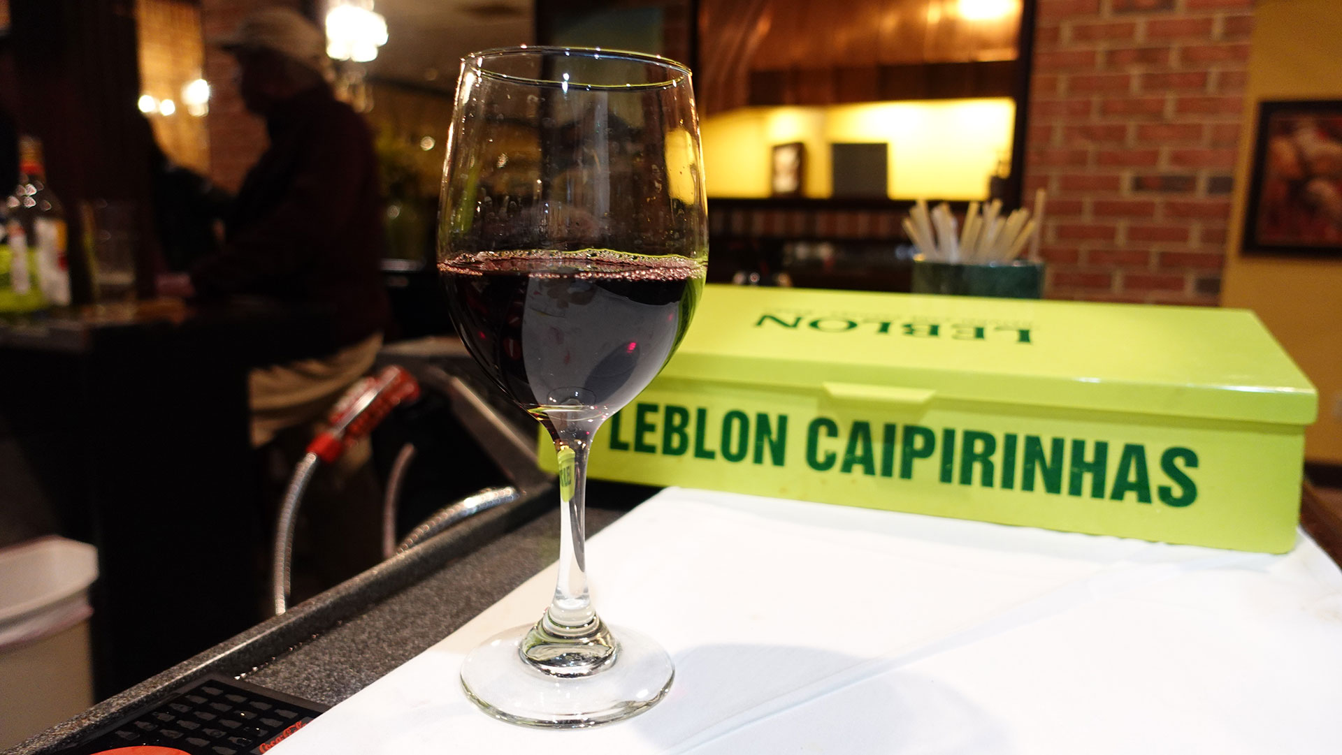 Glass of red wine beside Leblon Caipirinhas branded box at bar