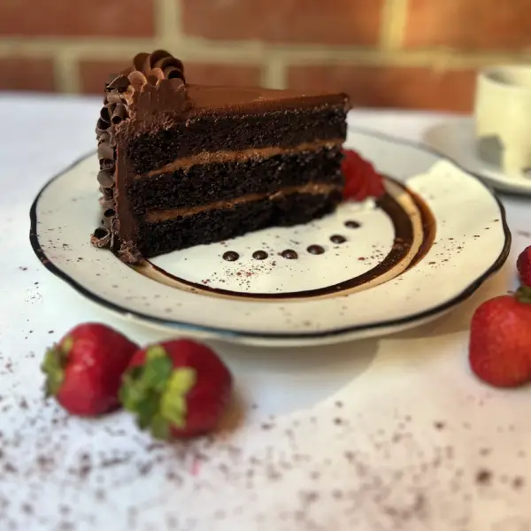 Slice of triple-layer chocolate cake with chocolate curls and strawberries