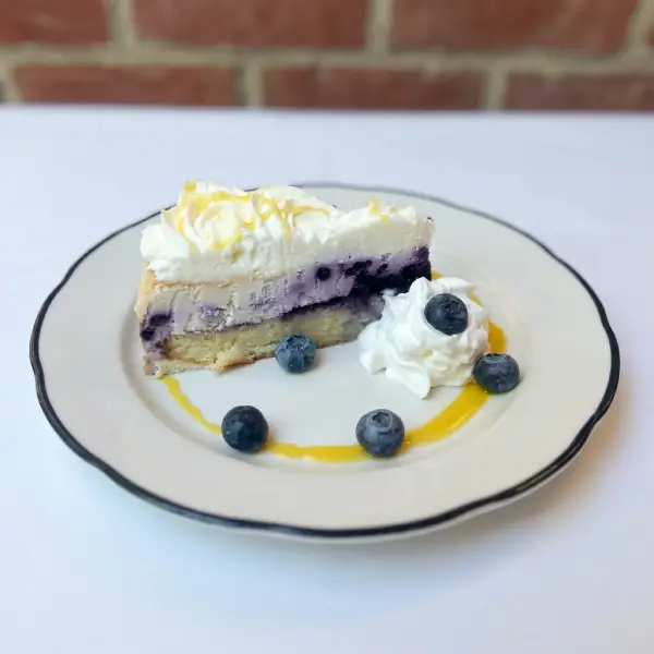 Slice of blueberry cheesecake with lemon drizzle and fresh blueberries